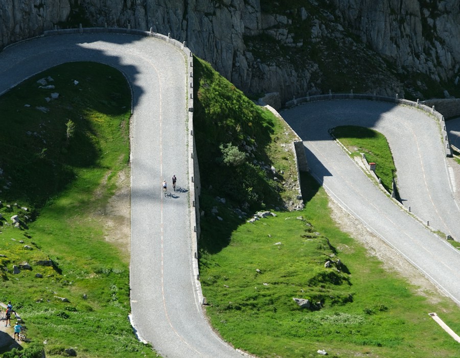 Cyclists climbing a serpentine alpine road above a valley.