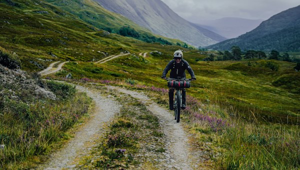 Gravel cyclist riding a track through a green mountain valley.